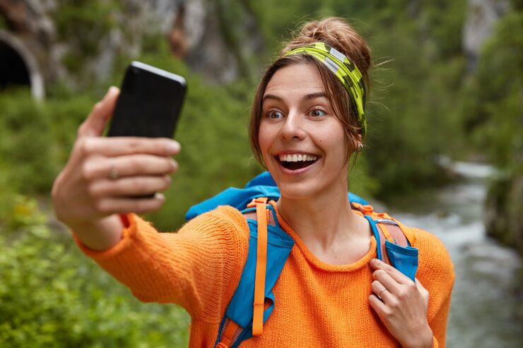 mirthful-tourist-with-broad-smile-holds-cell-phone-front-makes-selfie-portrait_273609-25979